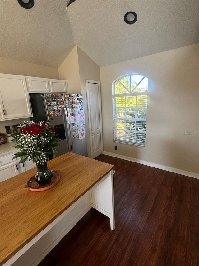 kitchen with stainless steel fridge, vaulted ceiling, white cabinets, and wooden counters