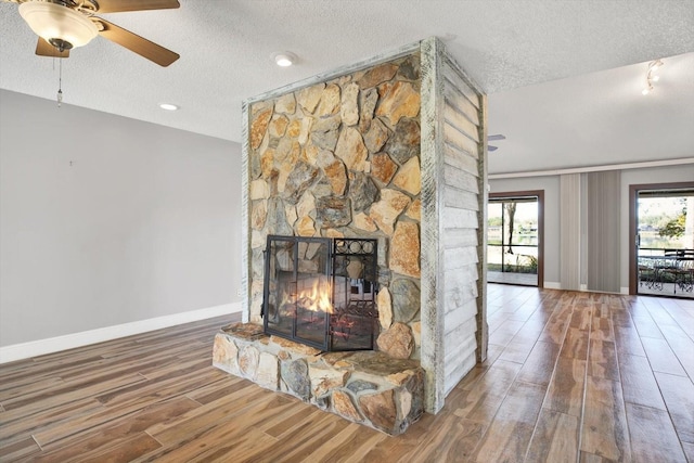 unfurnished living room with ceiling fan, a stone fireplace, wood-type flooring, and a textured ceiling