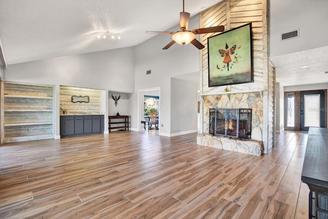 unfurnished living room featuring ceiling fan, a stone fireplace, high vaulted ceiling, and a textured ceiling