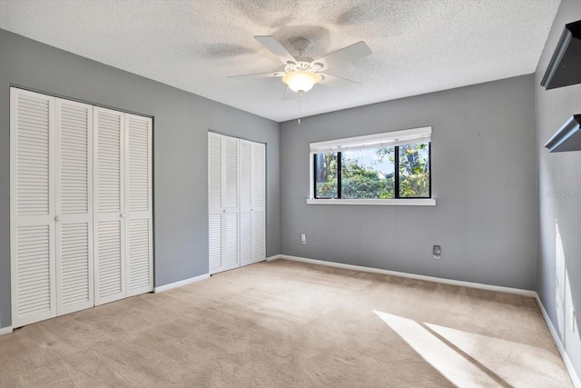 unfurnished bedroom with multiple closets, a textured ceiling, light colored carpet, and ceiling fan