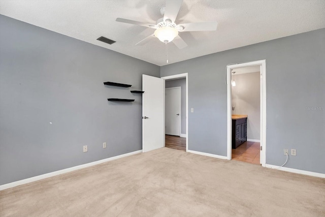 unfurnished bedroom featuring ceiling fan, light carpet, ensuite bath, and a textured ceiling