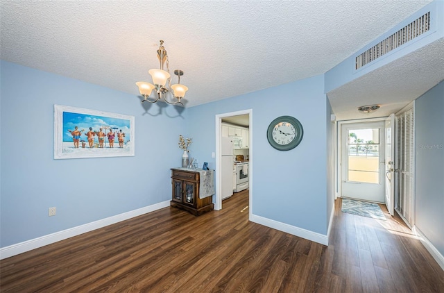 empty room featuring dark hardwood / wood-style flooring, a chandelier, and a textured ceiling