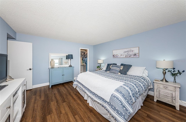 bedroom with a walk in closet, dark wood-type flooring, a textured ceiling, and a closet