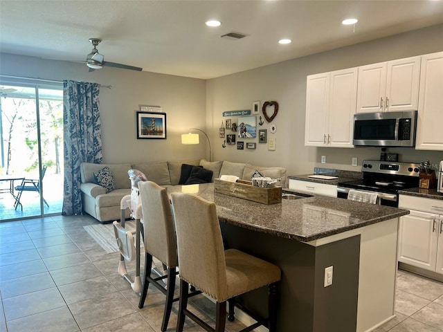 kitchen featuring a breakfast bar, appliances with stainless steel finishes, a center island, white cabinets, and dark stone counters