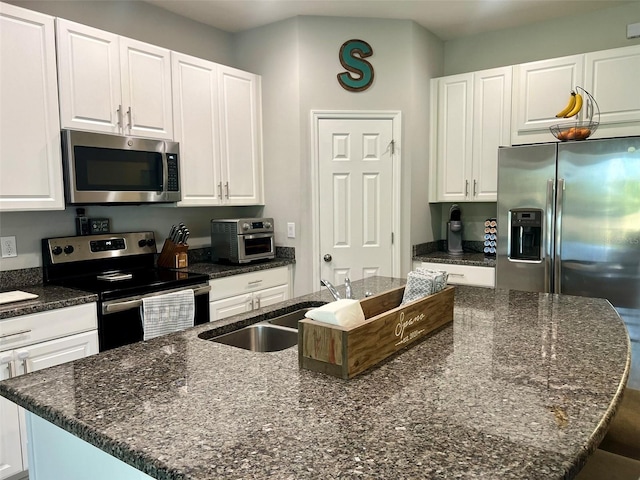 kitchen with appliances with stainless steel finishes, a kitchen island with sink, sink, and white cabinets