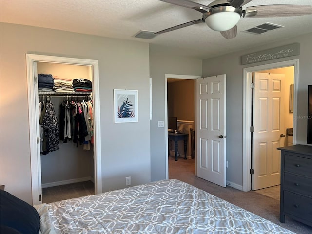 bedroom featuring a walk in closet, a textured ceiling, carpet floors, a closet, and ceiling fan