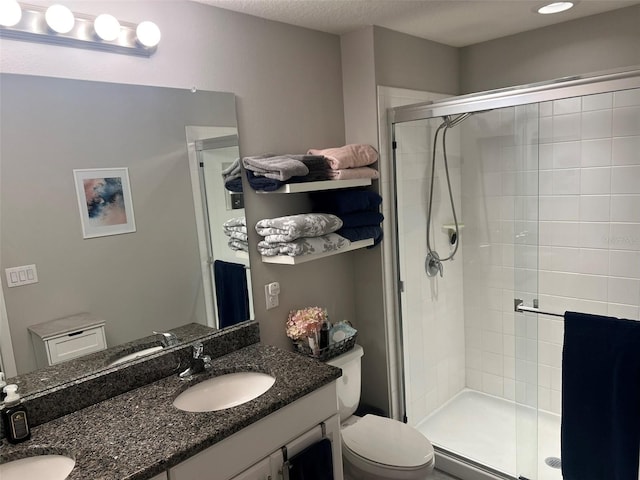 bathroom featuring vanity, toilet, a shower with shower door, and a textured ceiling