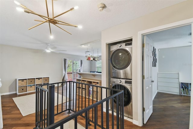 corridor featuring stacked washer / drying machine, dark hardwood / wood-style floors, a textured ceiling, and rail lighting