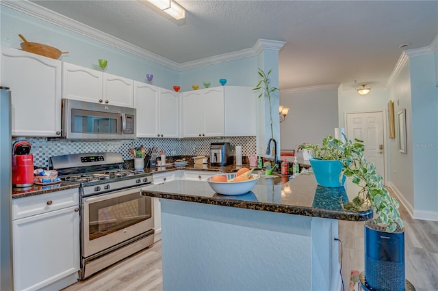 kitchen with crown molding, dark stone counters, backsplash, stainless steel appliances, and white cabinets