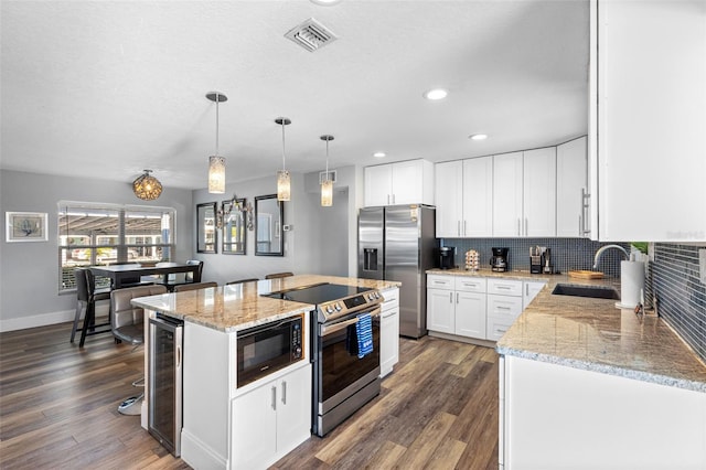 kitchen featuring appliances with stainless steel finishes, hanging light fixtures, white cabinets, a kitchen island, and beverage cooler