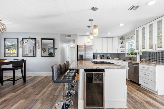 kitchen featuring wine cooler, white cabinetry, light stone counters, a center island, and appliances with stainless steel finishes