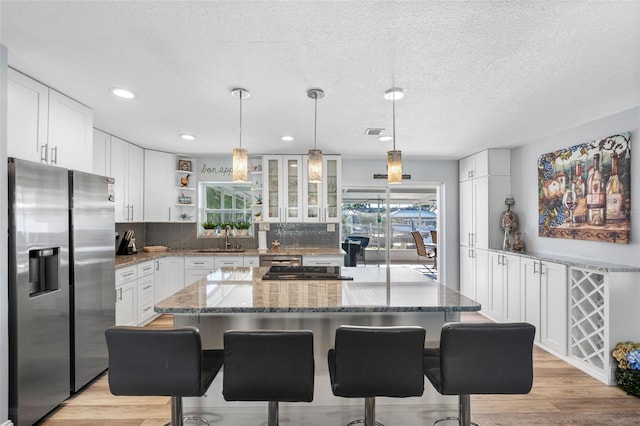 kitchen with a kitchen island, white cabinets, a kitchen breakfast bar, stainless steel appliances, and a textured ceiling