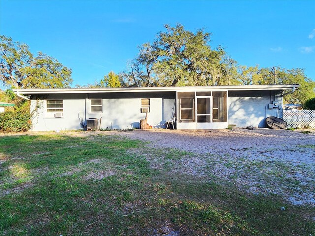 back of property with a sunroom, central air condition unit, stucco siding, and a lawn