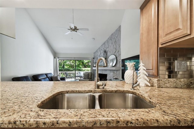 kitchen with sink, backsplash, light stone countertops, and ceiling fan