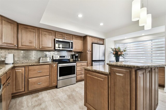 kitchen with stainless steel appliances, light stone counters, decorative backsplash, a kitchen island, and decorative light fixtures