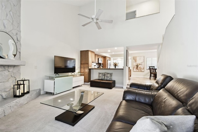 living room with ceiling fan, a towering ceiling, light carpet, and a fireplace