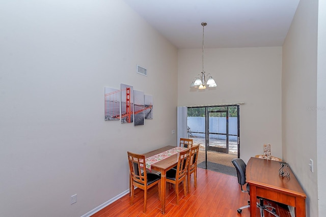 dining area featuring hardwood / wood-style flooring, a towering ceiling, and a notable chandelier