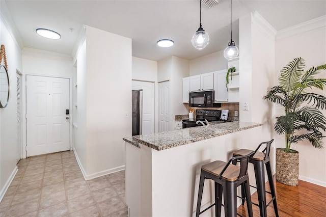 kitchen with white cabinetry, kitchen peninsula, pendant lighting, light stone countertops, and black appliances