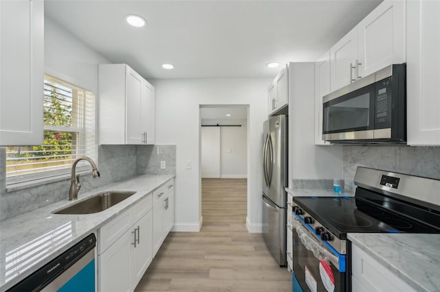 kitchen featuring white cabinetry, light stone countertops, a barn door, and appliances with stainless steel finishes