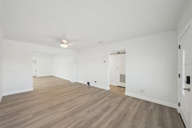 empty room featuring light hardwood / wood-style floors, a barn door, and ceiling fan