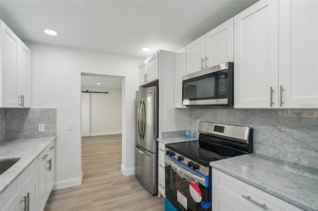 kitchen featuring white cabinetry, backsplash, light stone counters, stainless steel appliances, and a barn door