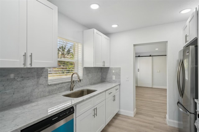 kitchen with sink, white cabinetry, appliances with stainless steel finishes, a barn door, and backsplash