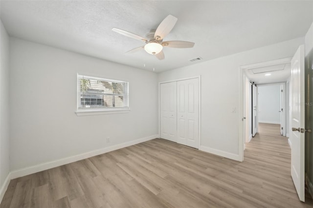 unfurnished bedroom featuring ceiling fan, a textured ceiling, a closet, and light wood-type flooring