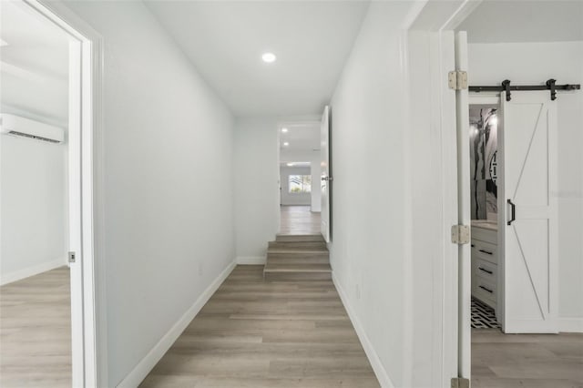 hall with a barn door, a wall mounted AC, and light hardwood / wood-style flooring