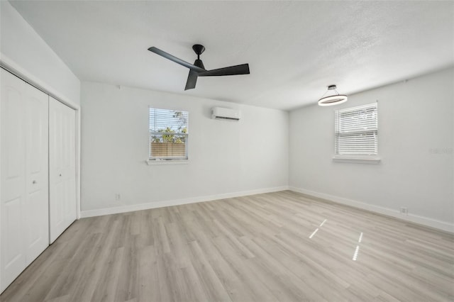 unfurnished bedroom featuring ceiling fan, a wall mounted AC, light hardwood / wood-style floors, a textured ceiling, and a closet