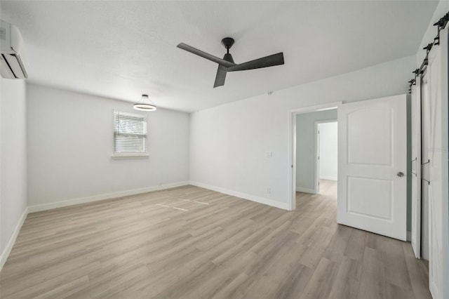 unfurnished room with light hardwood / wood-style flooring, a wall unit AC, a barn door, and ceiling fan