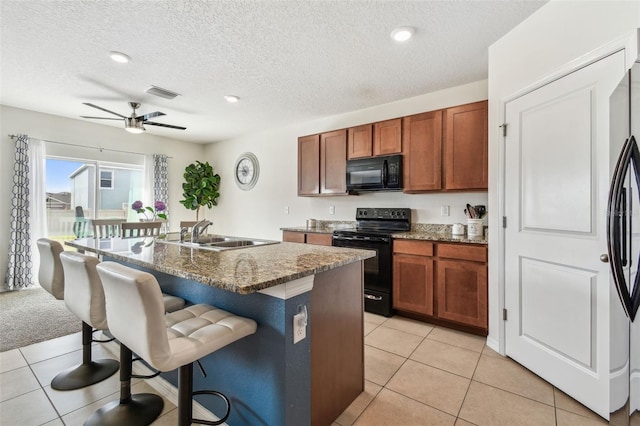 kitchen featuring an island with sink, sink, a kitchen breakfast bar, dark stone counters, and black appliances