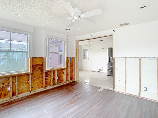 empty room featuring light wood-style flooring, visible vents, ceiling fan, and a textured ceiling