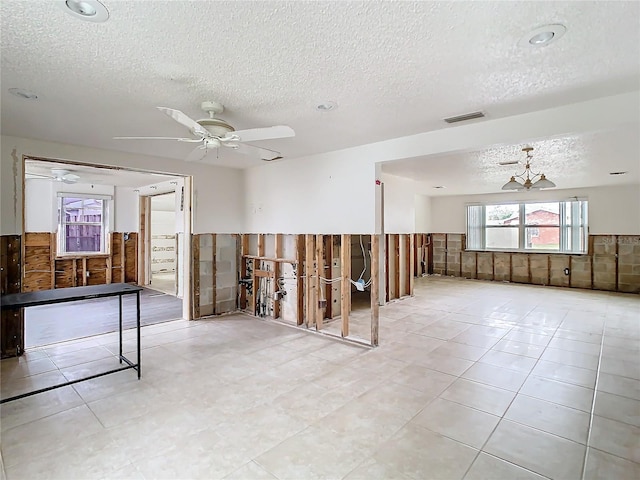 spare room with a wainscoted wall, visible vents, ceiling fan, and a textured ceiling