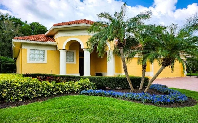 mediterranean / spanish-style home with a front yard, driveway, a tiled roof, and stucco siding