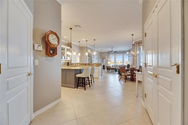 kitchen with a kitchen bar, hanging light fixtures, ornamental molding, light tile patterned floors, and light stone counters