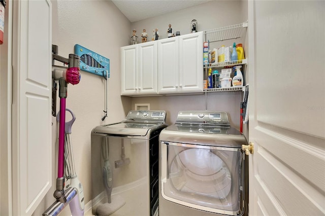 clothes washing area featuring a textured ceiling, cabinets, and washing machine and clothes dryer