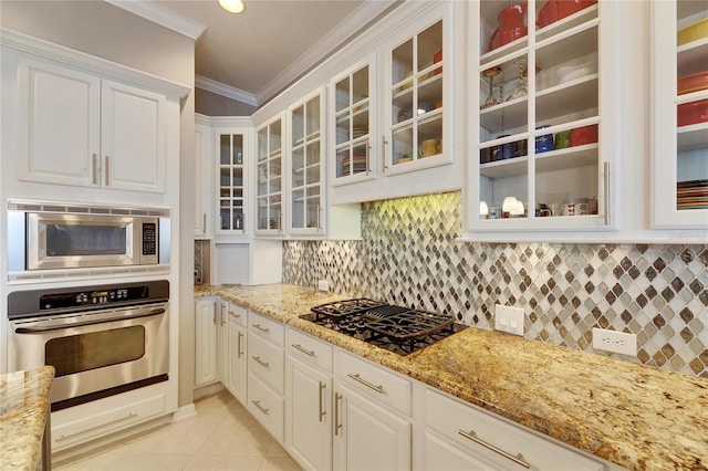 kitchen featuring light tile patterned flooring, white cabinetry, ornamental molding, light stone counters, and stainless steel appliances