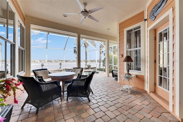 sunroom featuring ceiling fan and a water view