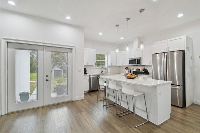 kitchen with a breakfast bar, appliances with stainless steel finishes, hanging light fixtures, a center island, and white cabinets