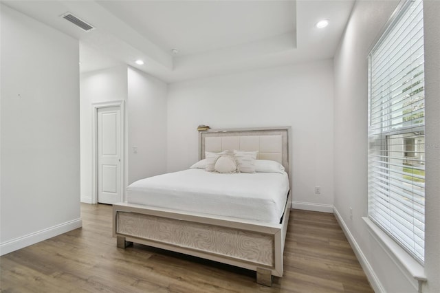 bedroom with hardwood / wood-style floors and a tray ceiling