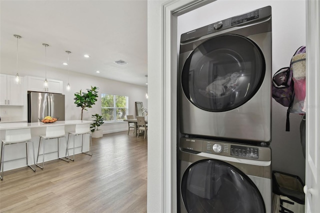 laundry room featuring stacked washer / dryer and light hardwood / wood-style flooring