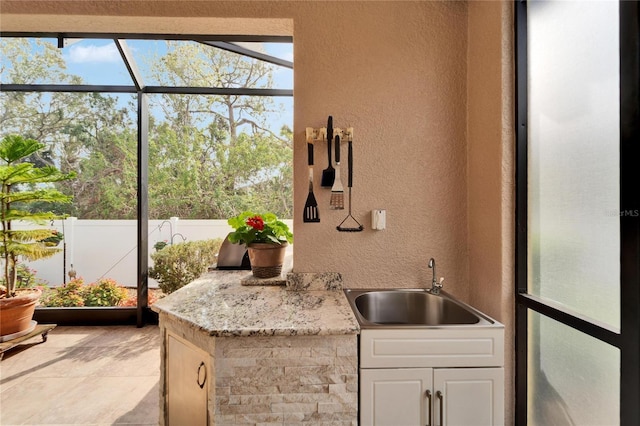 kitchen featuring light stone counters, sink, and white cabinets