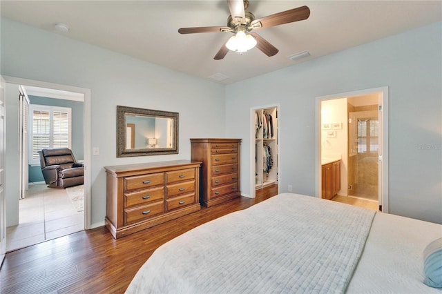 bedroom with dark hardwood / wood-style floors, connected bathroom, a walk in closet, ceiling fan, and a closet