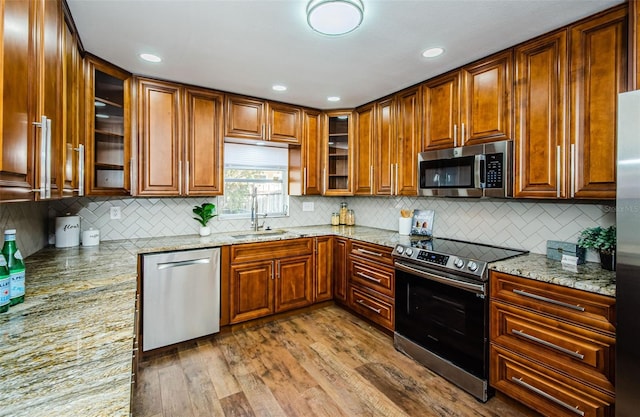 kitchen with sink, backsplash, light stone counters, stainless steel appliances, and light wood-type flooring