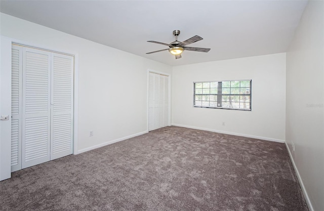 unfurnished bedroom featuring dark carpet, ceiling fan, and two closets