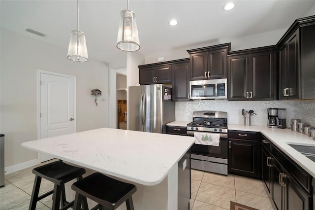 kitchen with a kitchen island, appliances with stainless steel finishes, a breakfast bar, decorative light fixtures, and decorative backsplash