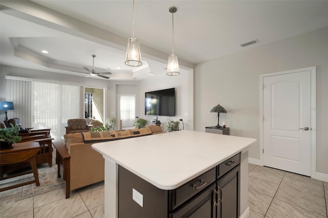 kitchen featuring a kitchen island, hanging light fixtures, ceiling fan, a raised ceiling, and dark brown cabinets