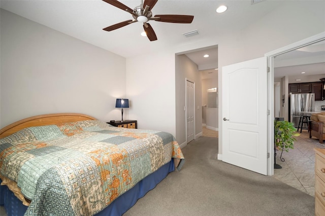 bedroom with connected bathroom, light colored carpet, stainless steel fridge, a closet, and ceiling fan