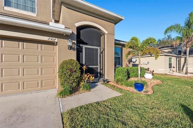 entrance to property featuring a yard, an attached garage, and stucco siding