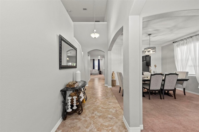 corridor featuring baseboards, arched walkways, and light colored carpet